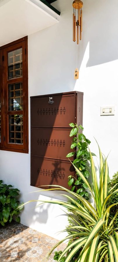 Coffee Brown three-tier steel shoe rack wall-mounted on a white veranda wall beside a wooden window, tiled floor clear below