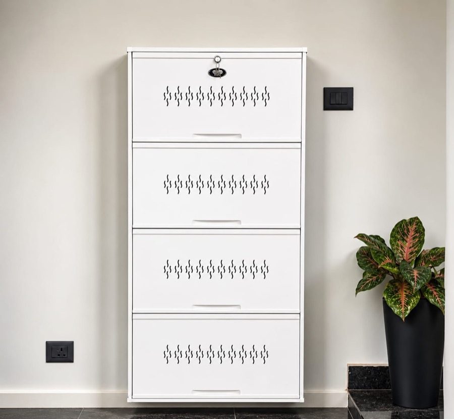 Ivory White four-tier steel shoe rack fitted flush to a hallway wall between a light switch and a socket, dark stone floor below